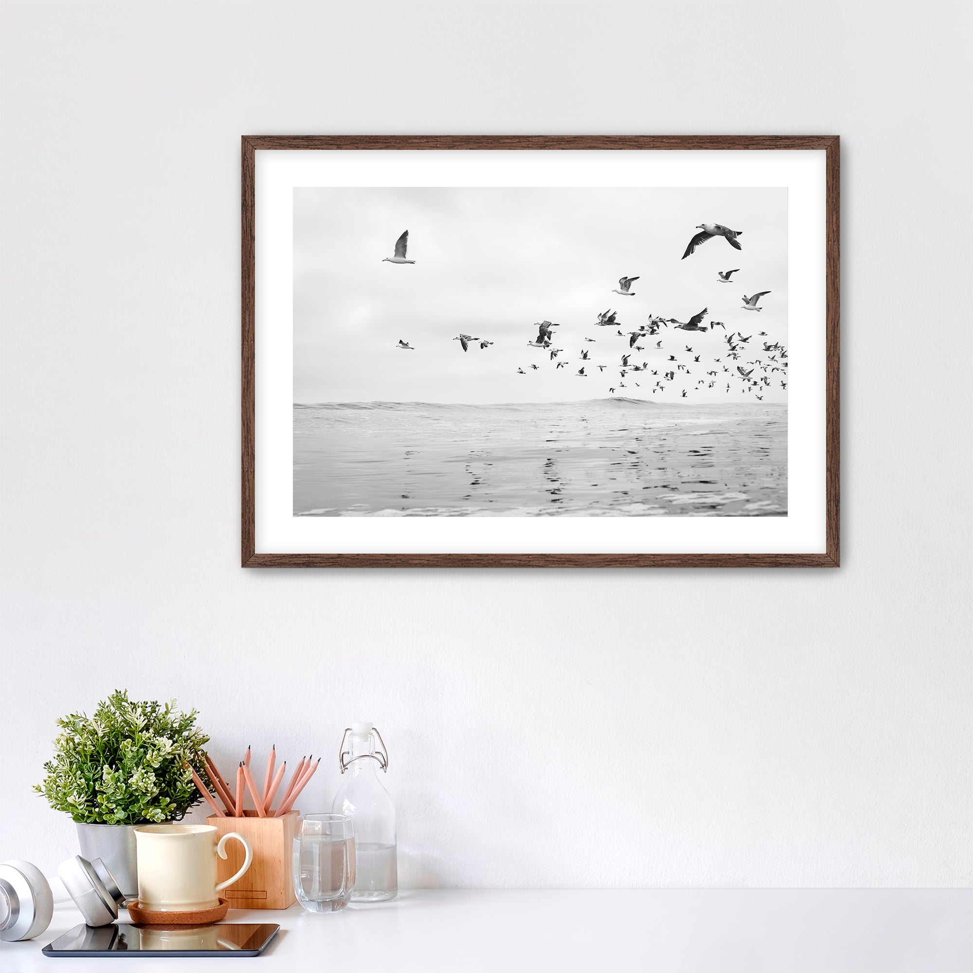 Framed artwork of birds flying over water on a white wall above a desk. Tamarack Beach, Carlsbad, California. 