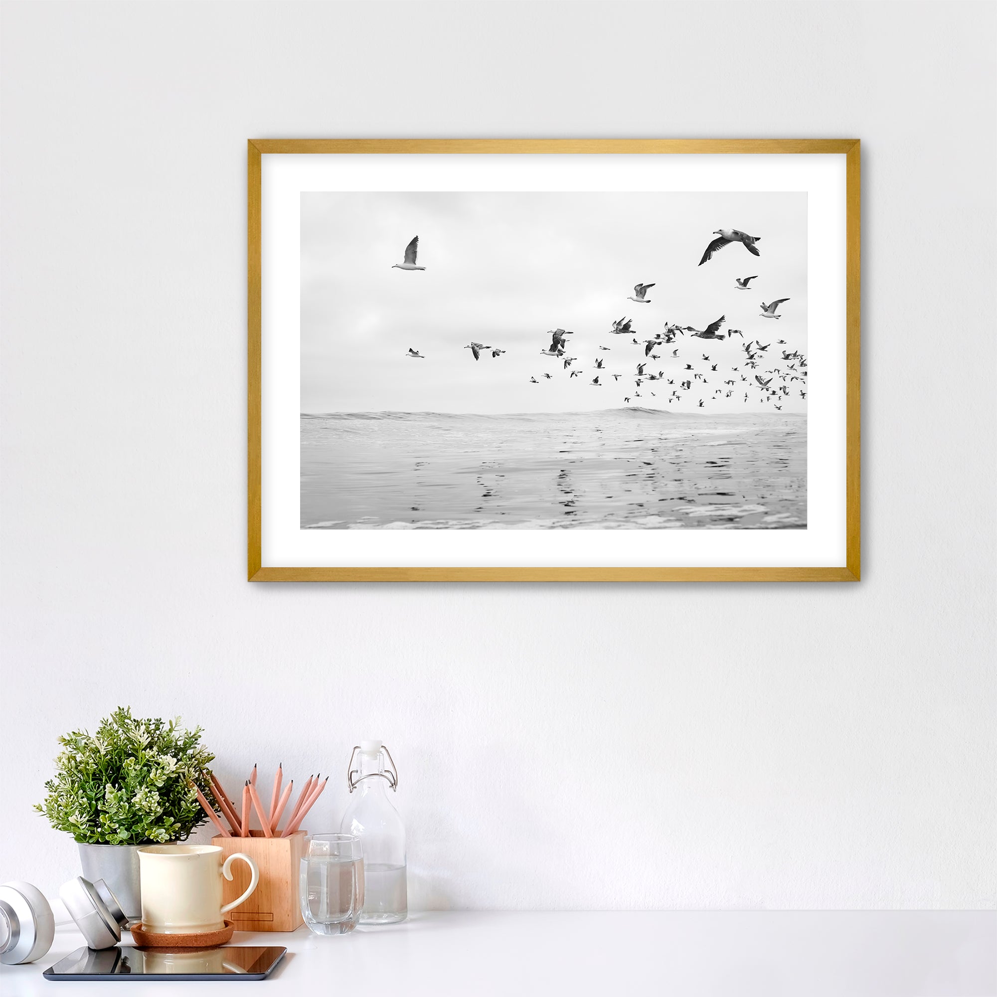 Framed artwork of birds flying over water on a white wall above a desk. Tamarack Beach, Carlsbad, California. 
