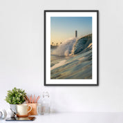Framed photograph of a beach scene with waves crashing in front of the historic Carlsbad power plant on a white wall above a desk.