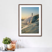 Framed photograph of a beach scene with waves crashing in front of the historic Carlsbad power plant on a white wall above a desk.