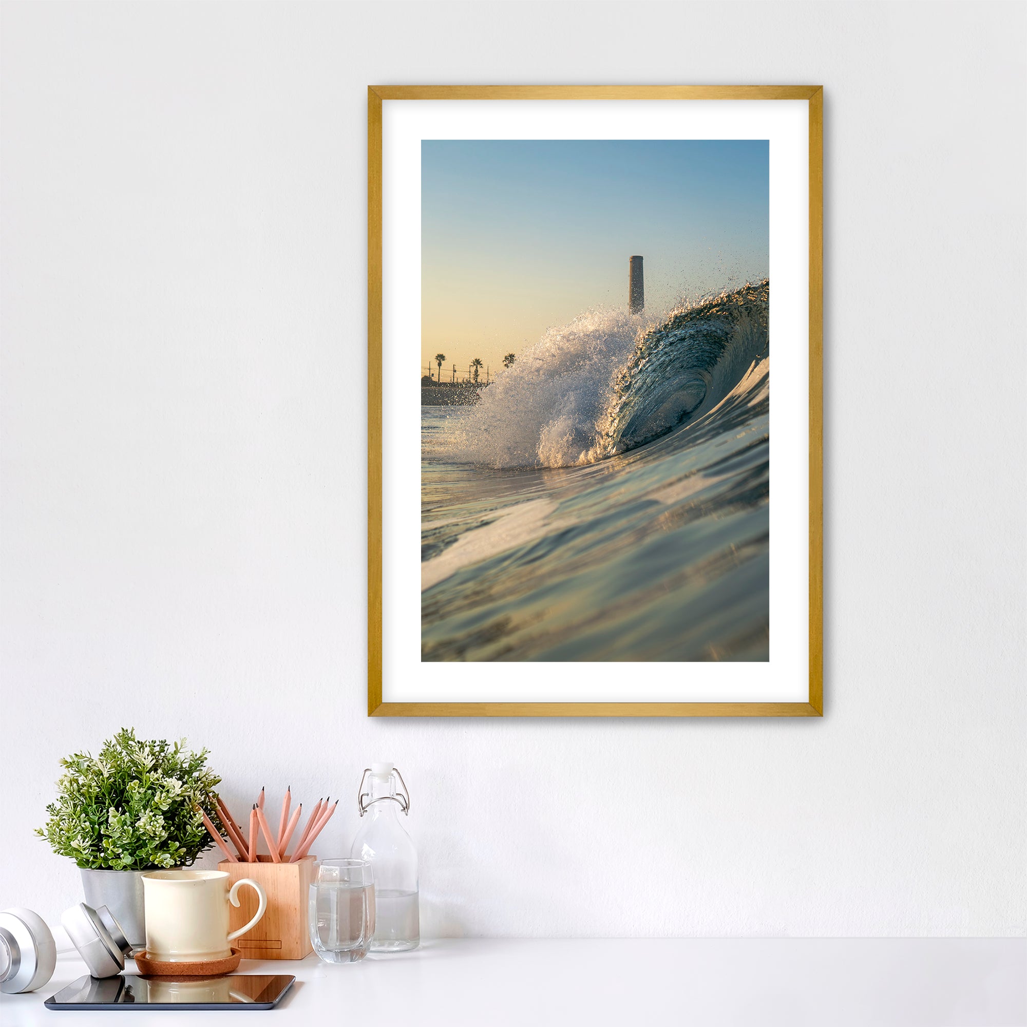Framed photograph of a beach scene with waves crashing in front of the historic Carlsbad power plant on a white wall above a desk.