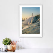 Framed photograph of a beach scene with waves crashing in front of the historic Carlsbad power plant on a white wall above a desk.