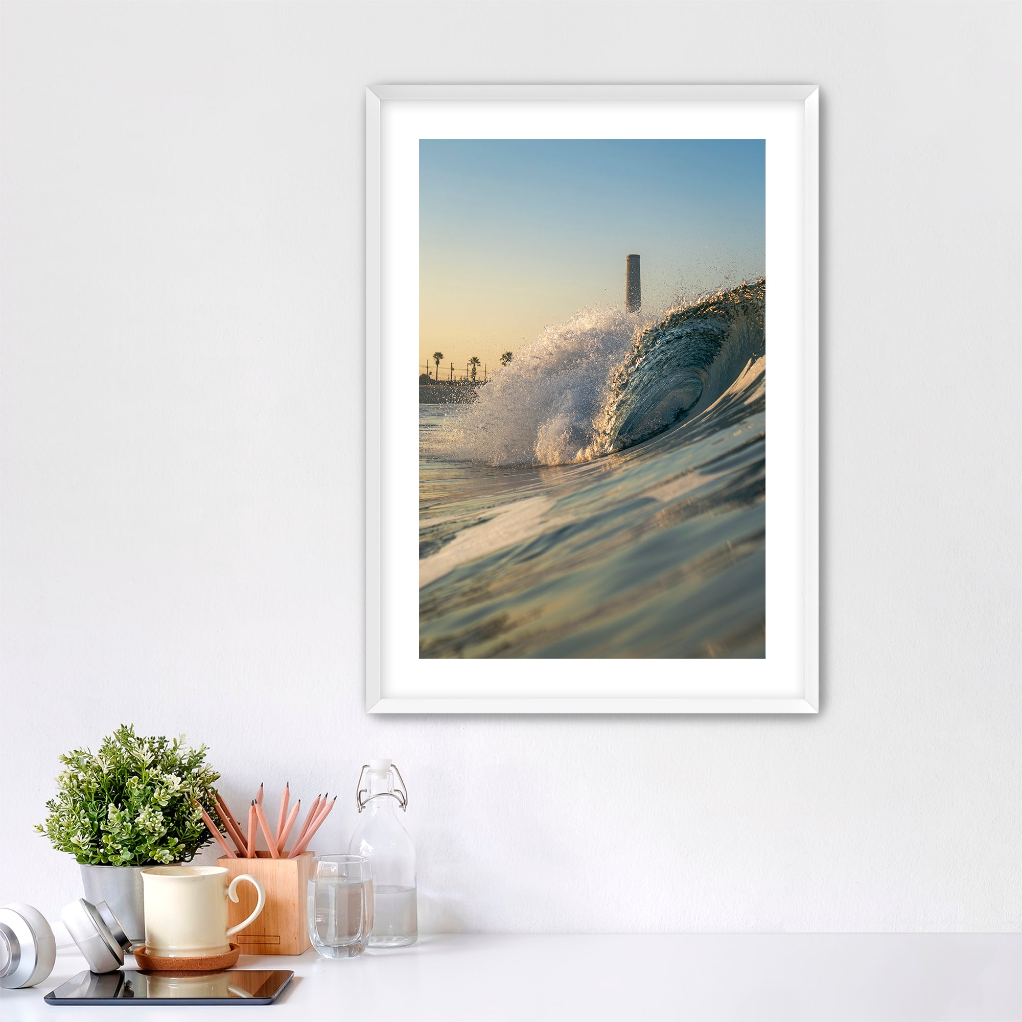Framed photograph of a beach scene with waves crashing in front of the historic Carlsbad power plant on a white wall above a desk.