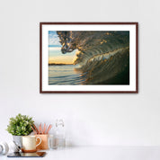 Framed artwork of a barreling wave on a wall above a desk with office supplies.