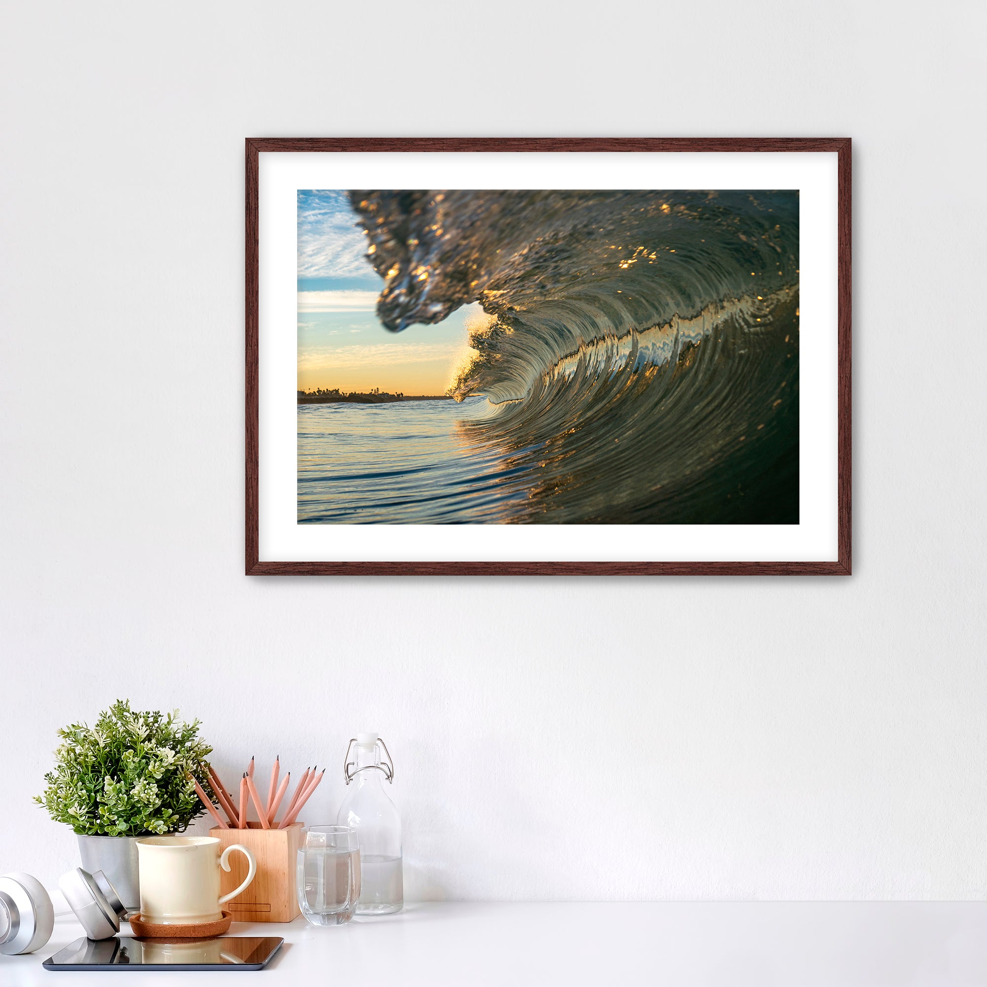 Framed artwork of a barreling wave on a wall above a desk with office supplies.