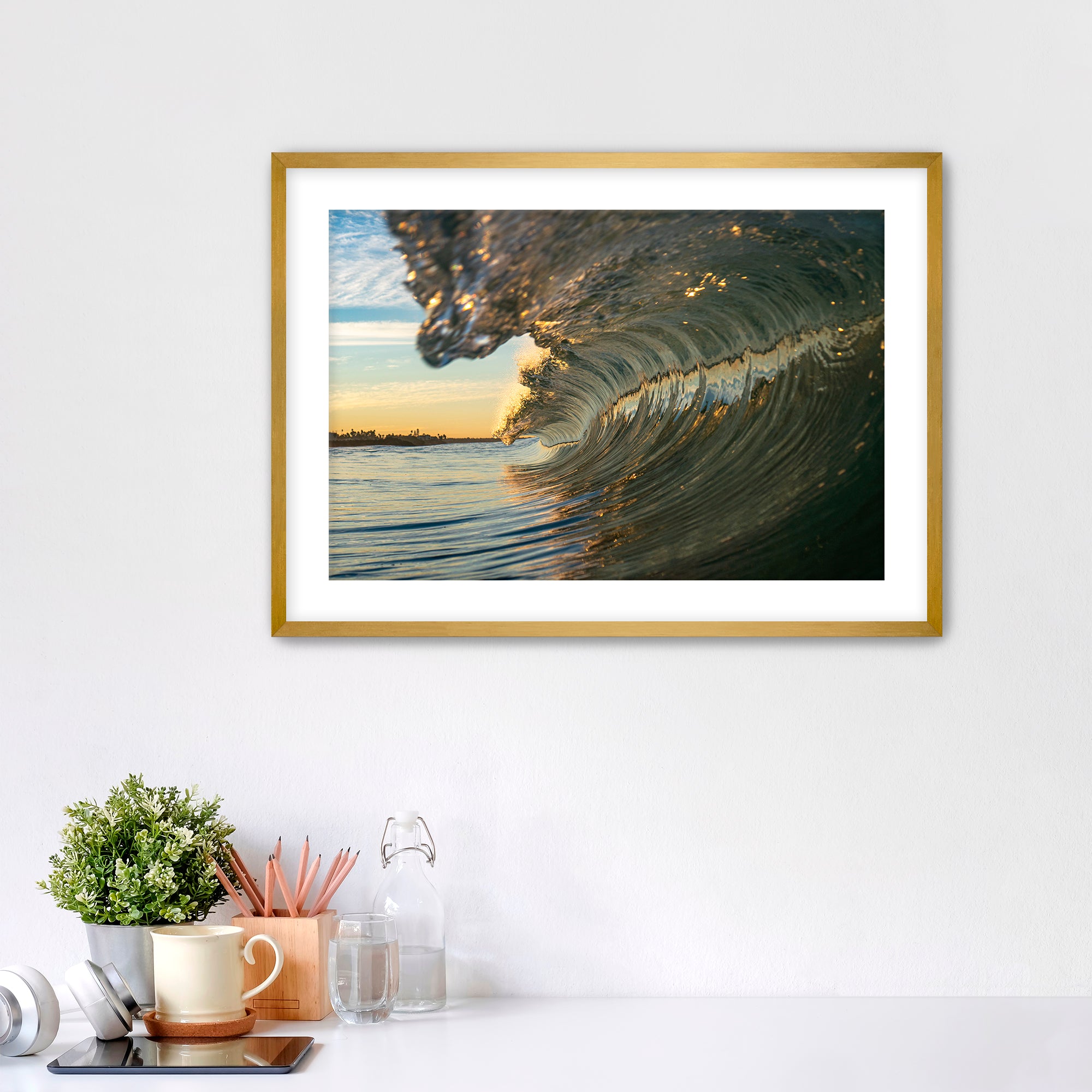 Framed artwork of a barreling wave on a wall above a desk with office supplies.