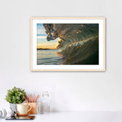 Framed artwork of a barreling wave on a wall above a desk with office supplies.