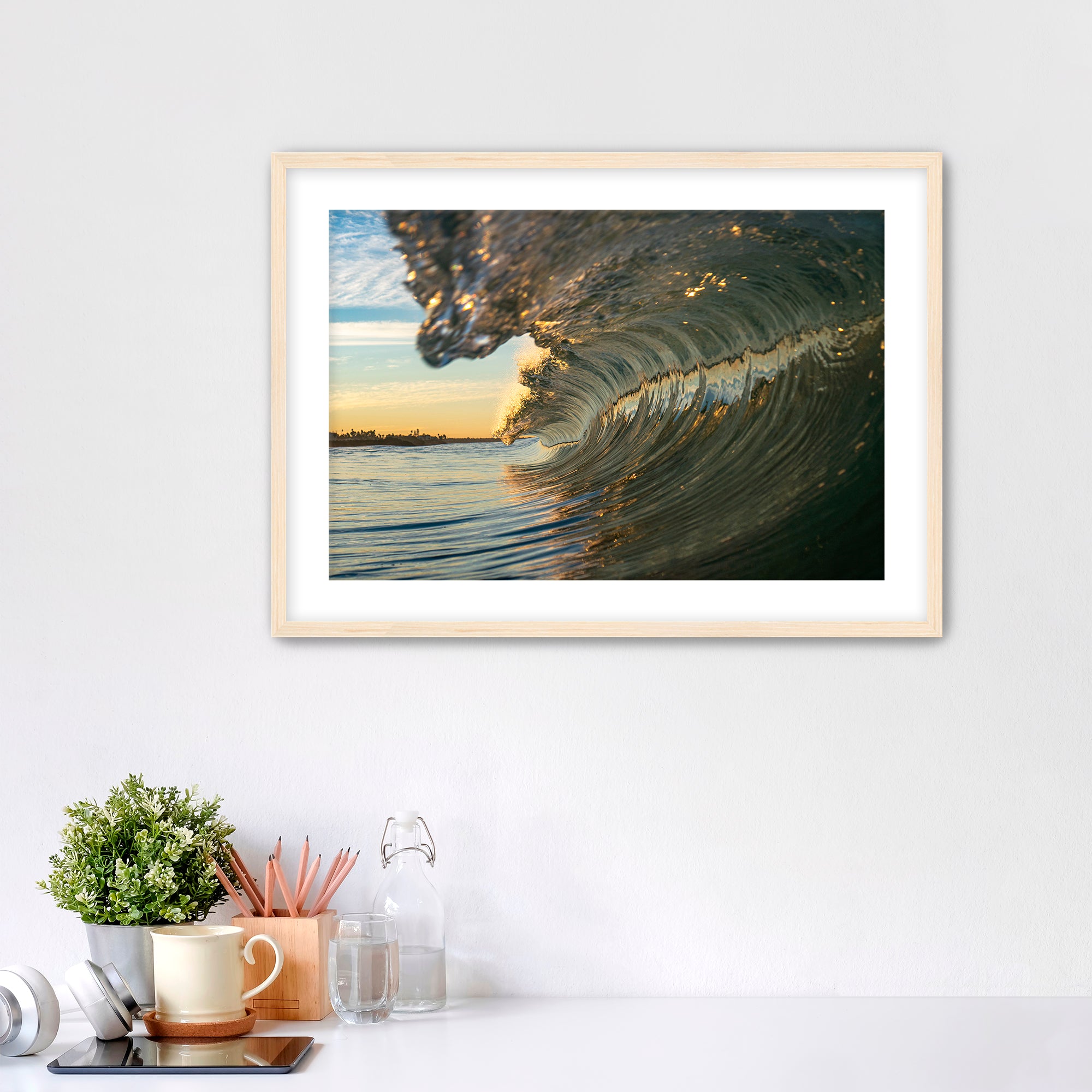 Framed artwork of a barreling wave on a wall above a desk with office supplies.