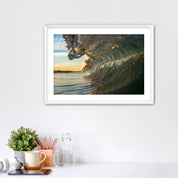 Framed artwork of a barreling wave on a wall above a desk with office supplies.