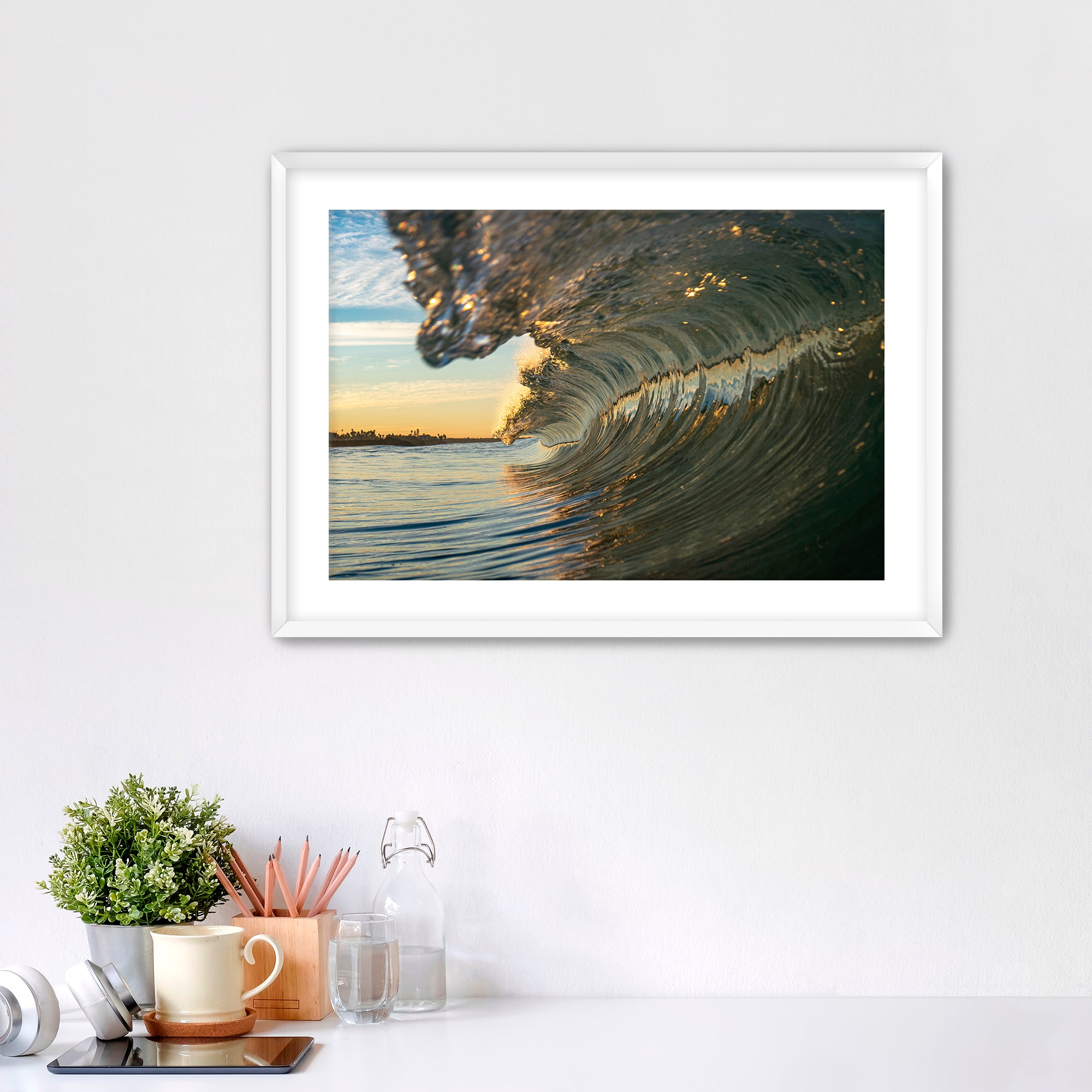 Framed artwork of a barreling wave on a wall above a desk with office supplies.