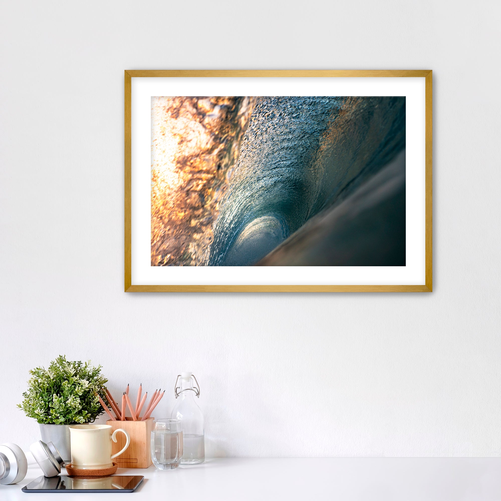 Framed photograph of the inside of a barreling wave on a white wall above a desk with office supplies.