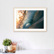 Framed photograph of the inside of a barreling wave on a white wall above a desk with office supplies.
