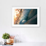 Framed photograph of the inside of a barreling wave on a white wall above a desk with office supplies.