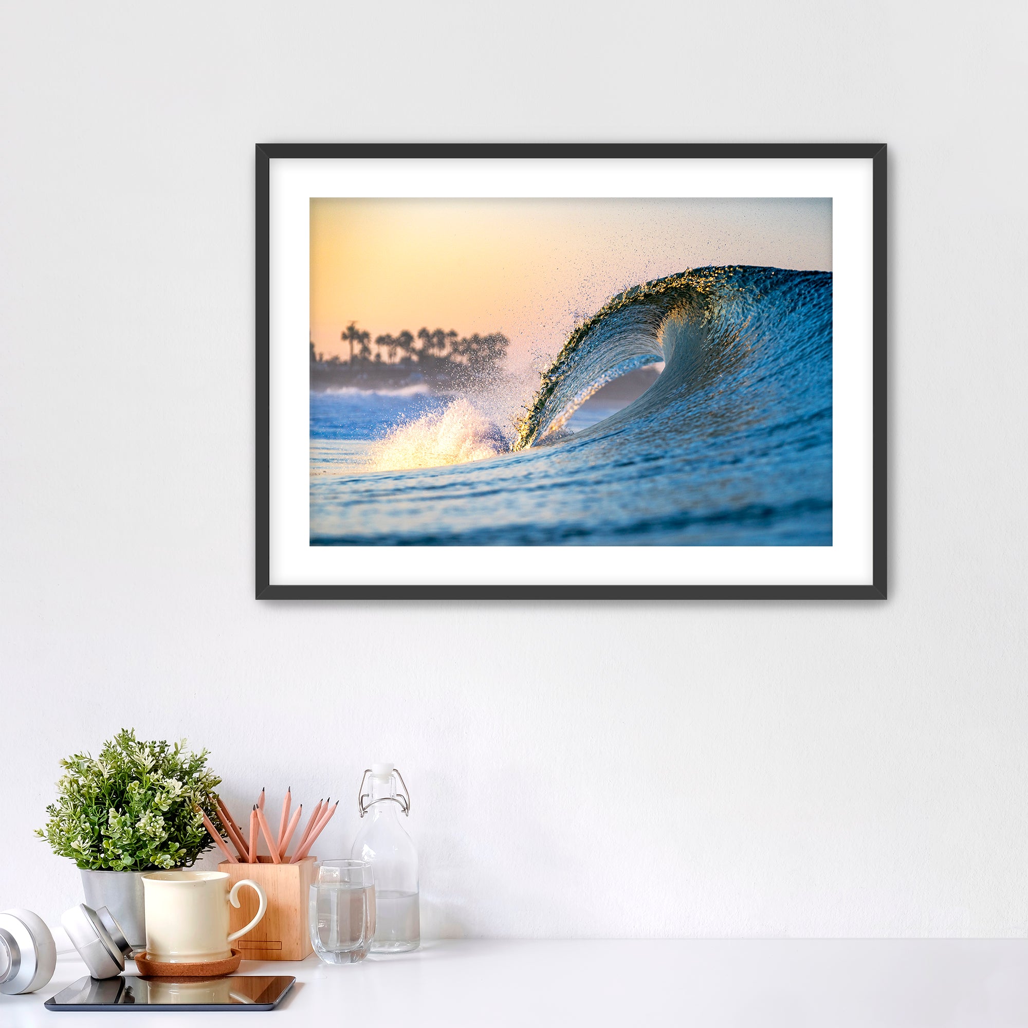 Framed photo of a wave crashing like a waterfall with a sunrise and palm trees in the background. 
