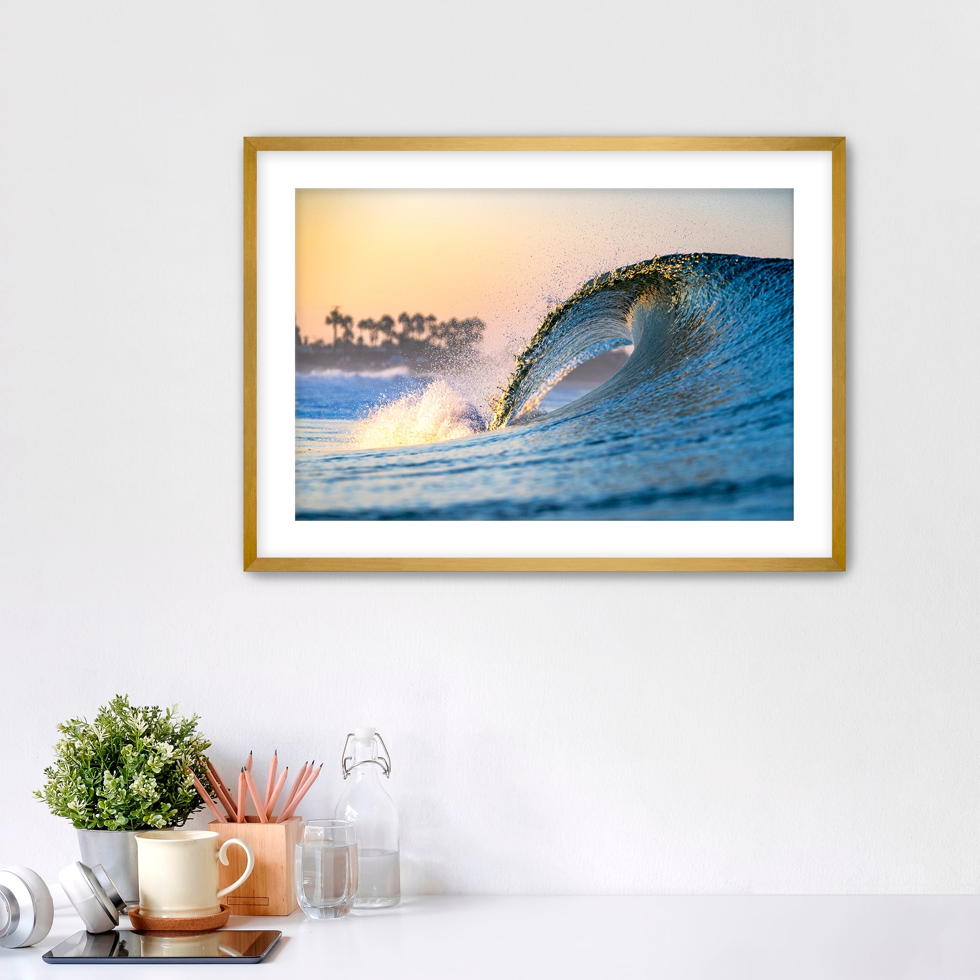 Framed photo of a wave crashing like a waterfall with a sunrise and palm trees in the background. 