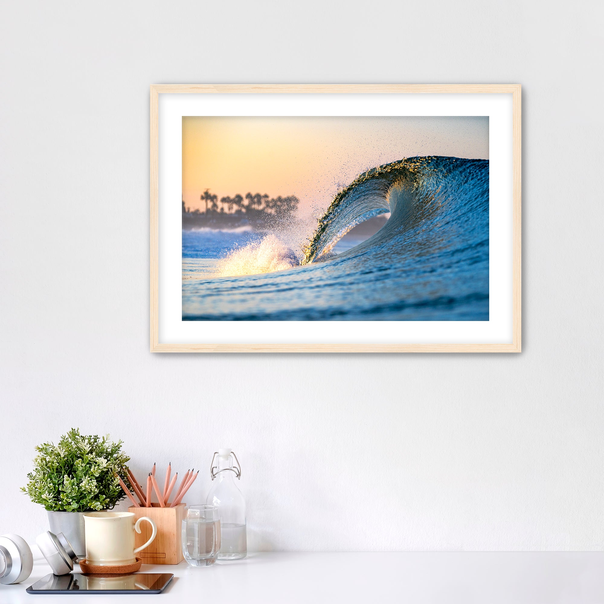 Framed photo of a wave crashing like a waterfall with a sunrise and palm trees in the background. 