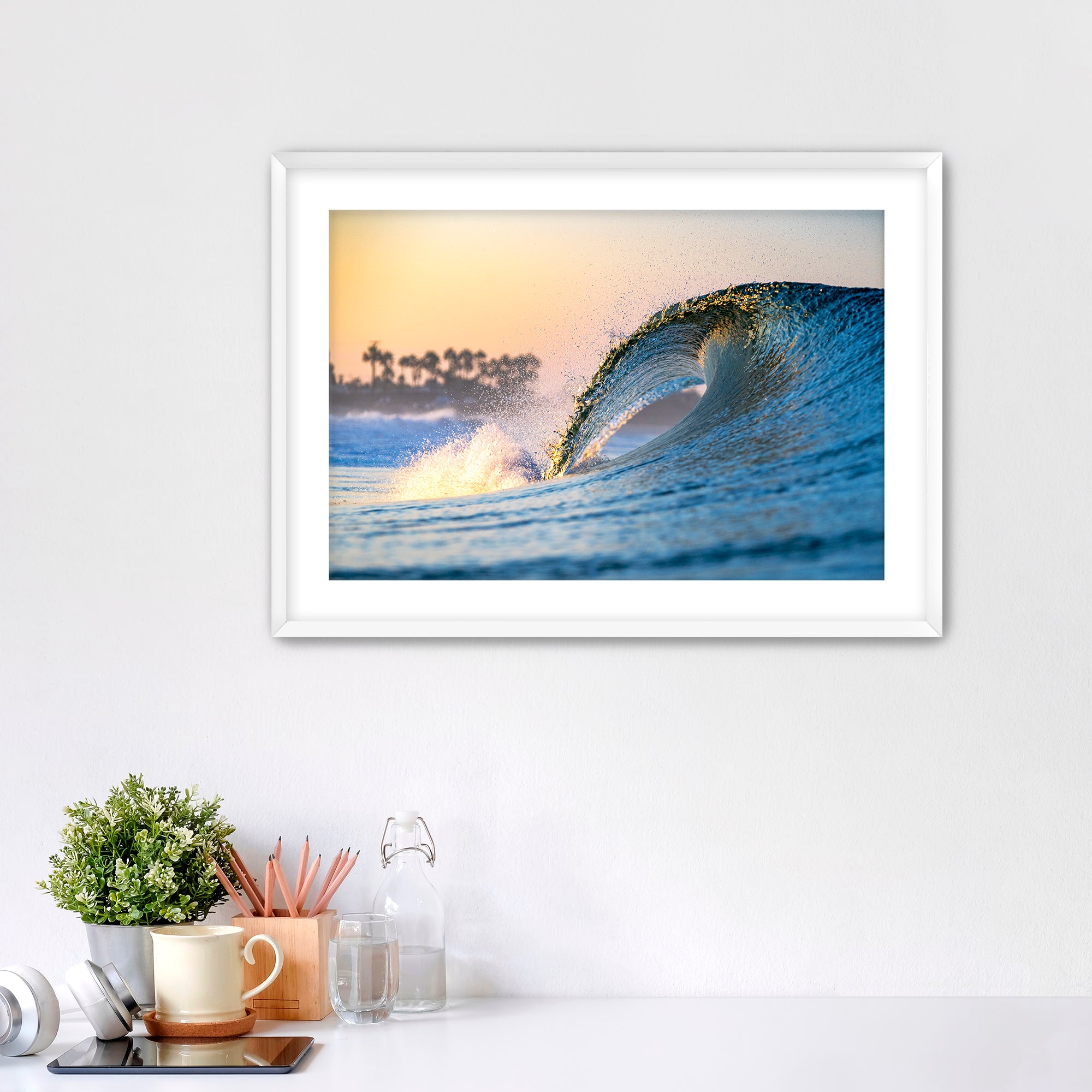 Framed photo of a wave crashing like a waterfall with a sunrise and palm trees in the background. 