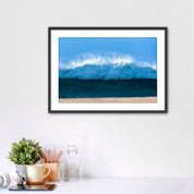 Framed artwork of a light blue wave on a beach with office items below. 