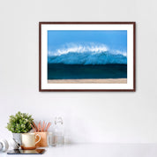 Framed artwork of a light blue wave on a beach with office items below. 