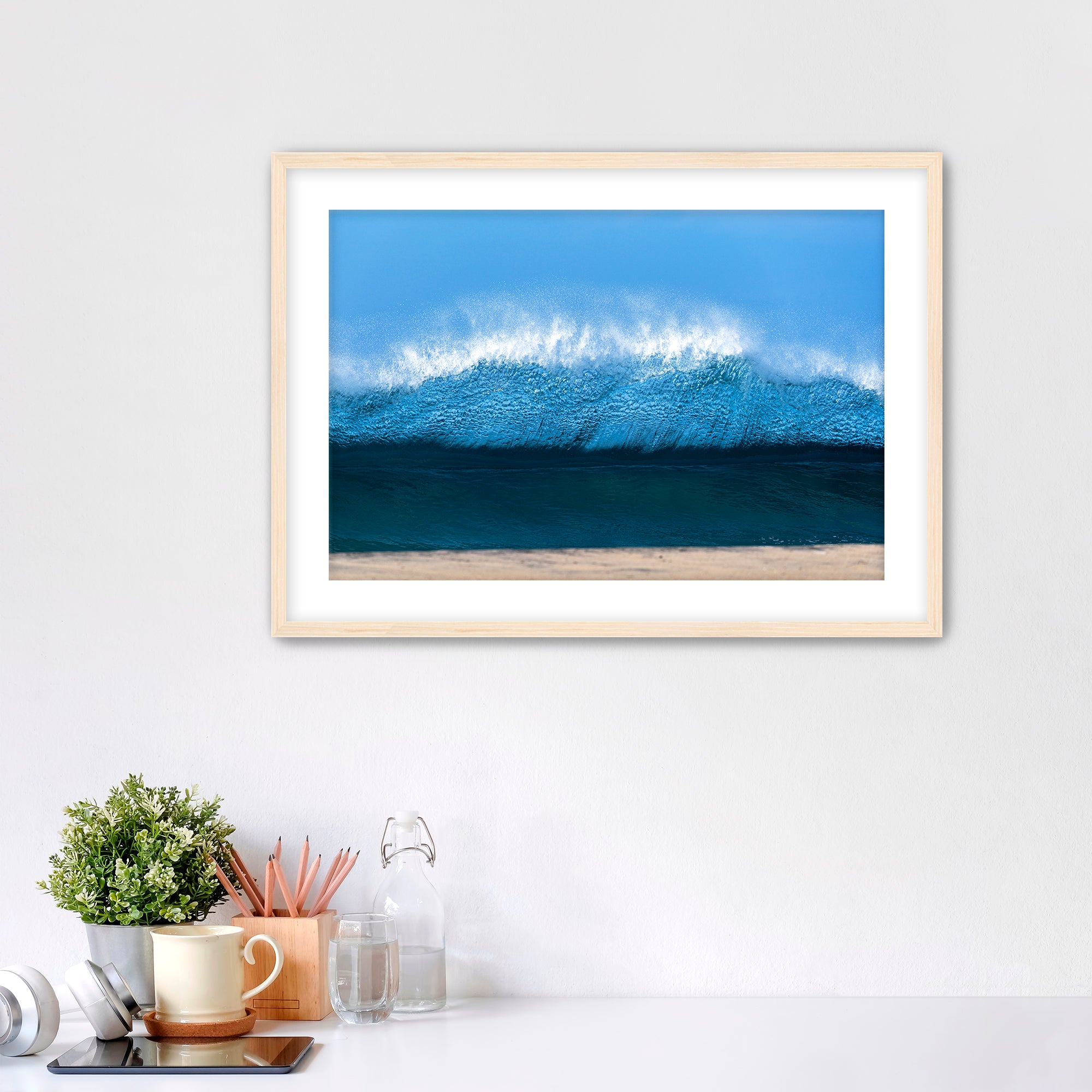 Framed artwork of a light blue wave on a beach with office items below. 