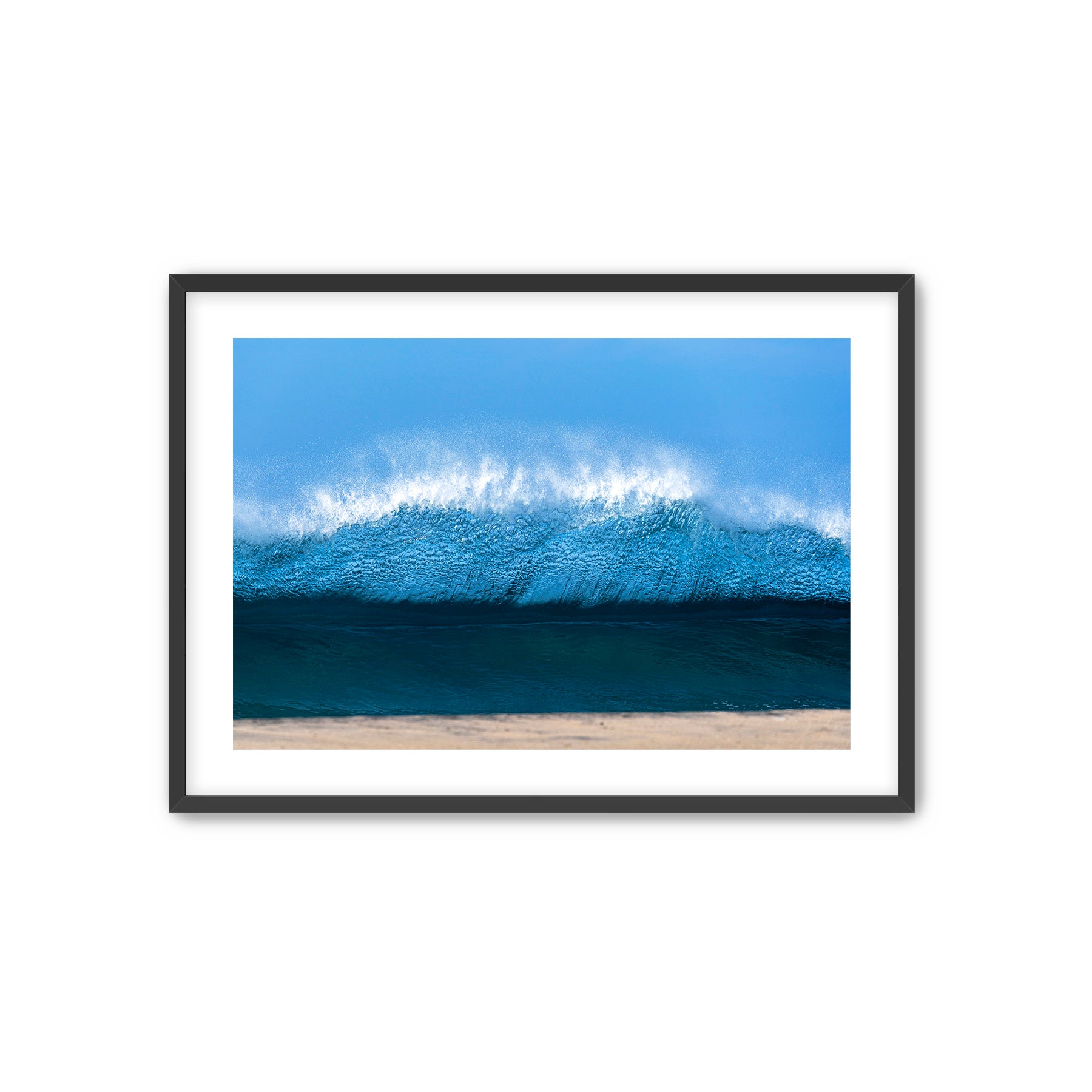 Framed photograph of a wave crashing onto a beach with a clear blue sky.